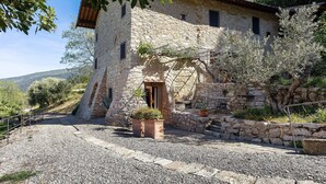 Un edificio in pietra con esterno rustico, un vialetto sterrato e un piccolo giardino con piante in vaso.