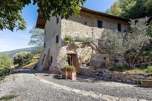 Ein Steinhaus mit rustikalem ĂuĂeren, einer Schotterauffahrt und einem kleinen Garten mit Blumentöpfen.