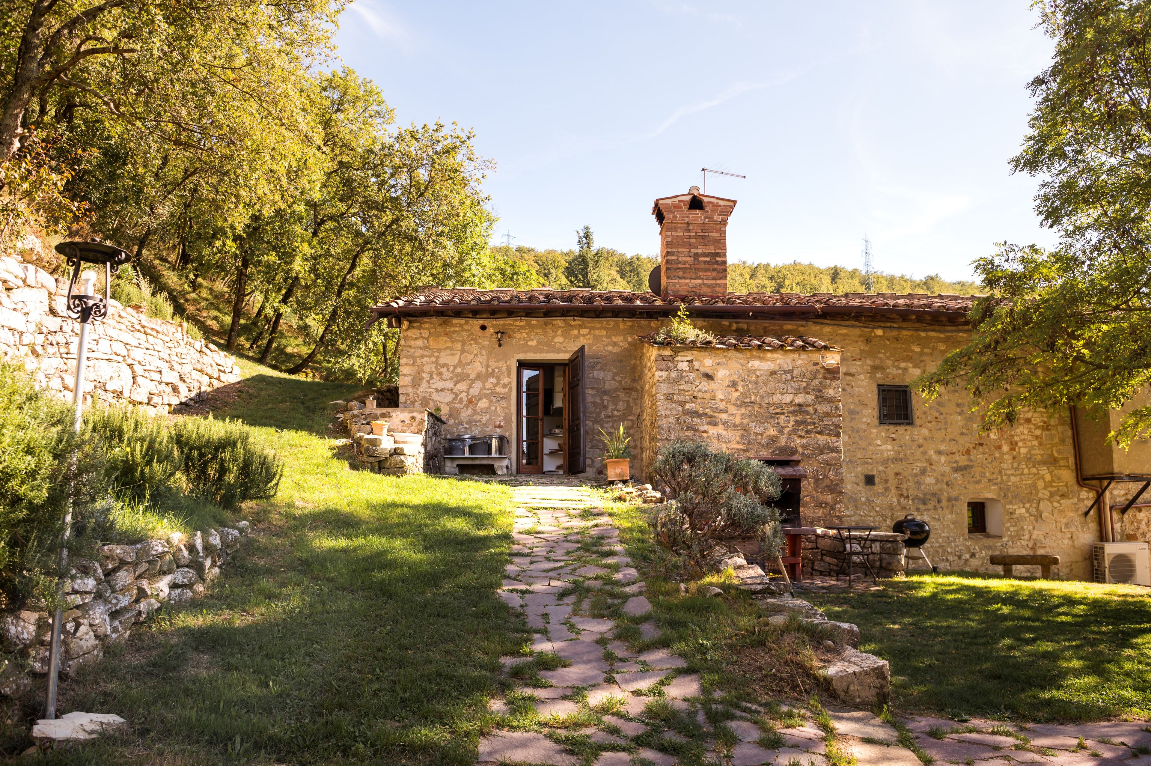 A stone building with a tiled roof, a chimney, and a paved pathway leading to the entrance.