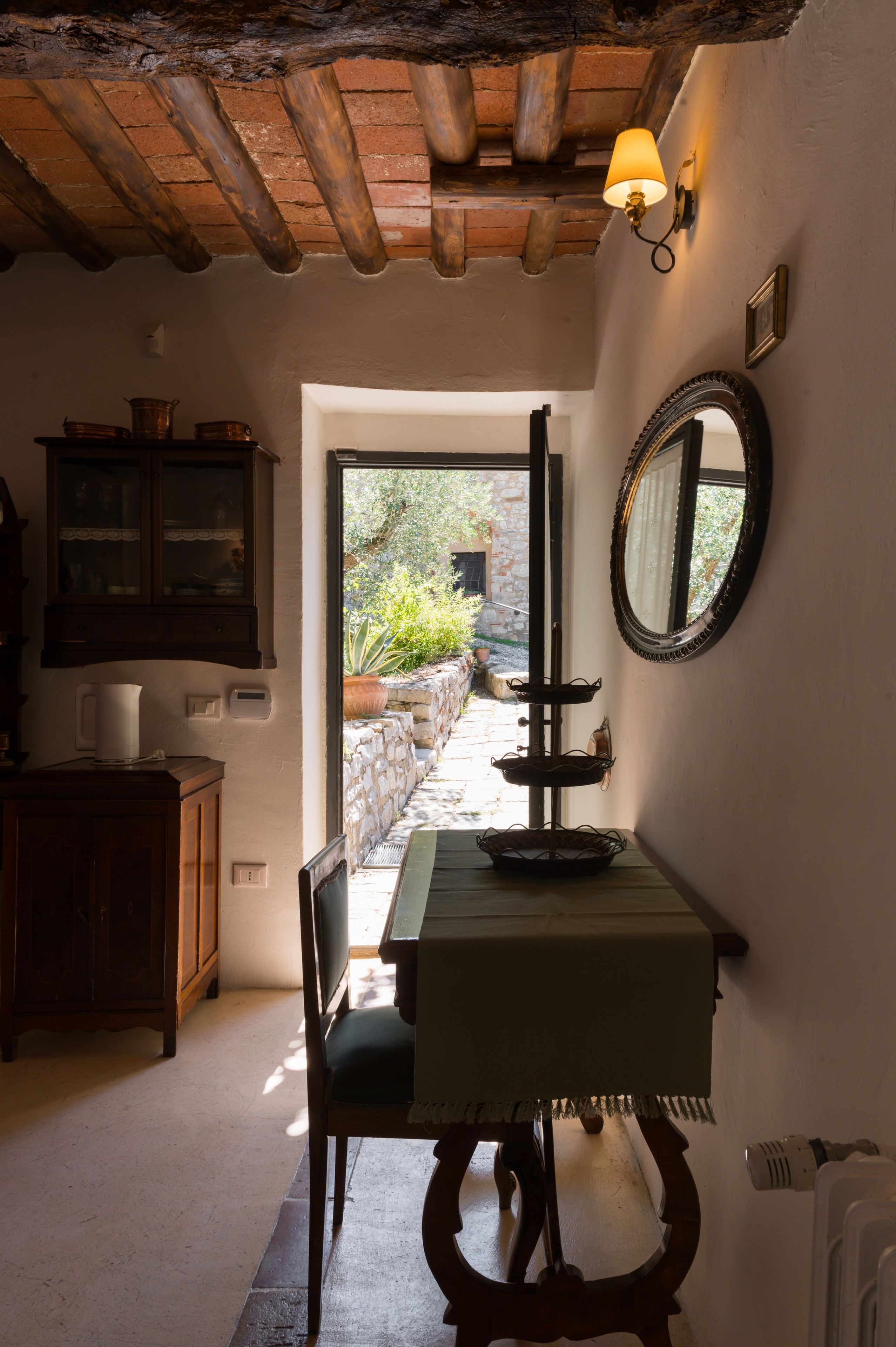 A narrow hallway with a wooden ceiling, a table with a candle, a mirror, and a cabinet with a pitcher.
