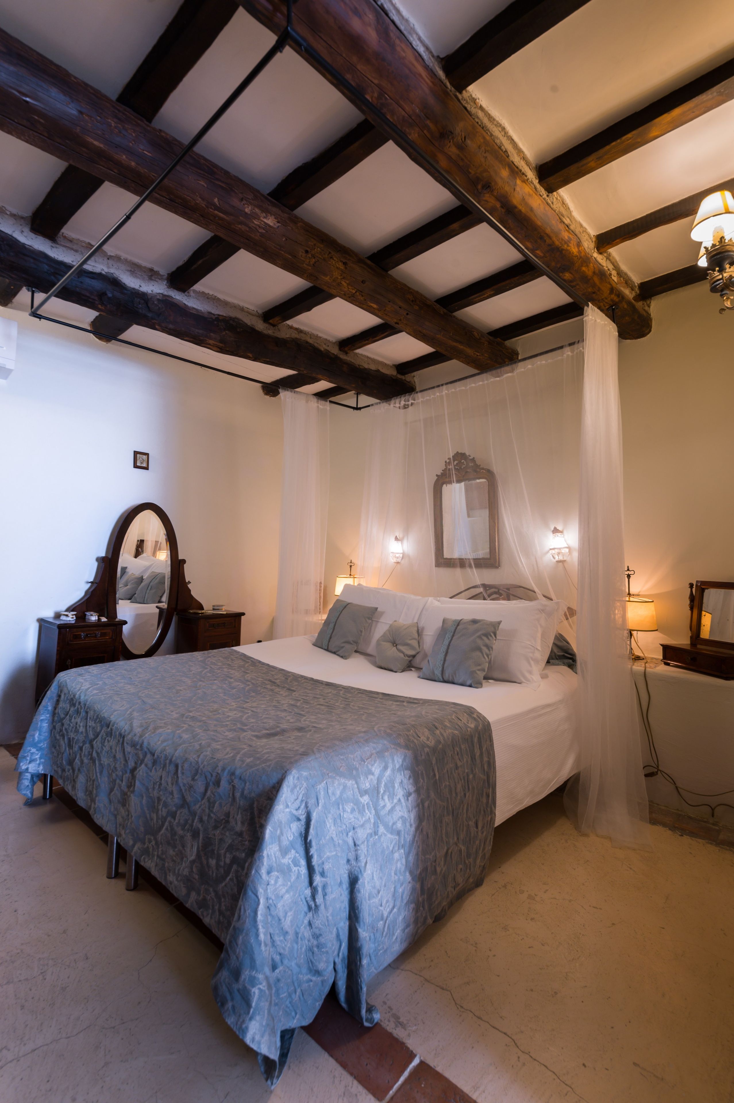 A bedroom with a bed, bedside lamps, a mirror, and a wooden ceiling.