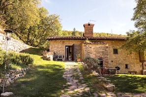 Un edificio rústico de piedra con tejado de baldosas, una chimenea y un camino de piedra que conduce a la entrada.