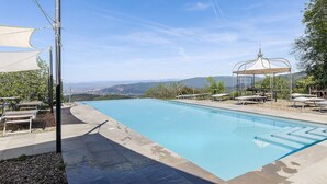 Una piscina con vista su montagne lontane, un padiglione e sedie a sdraio.