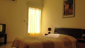 A bedroom with a bed, a nightstand, a lamp, a window with curtains, and a wall-mounted picture. - Rental apartment T2, 53m2 à Corte in quiet residence (Corte)