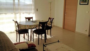 A dining area with a round table and four chairs, a window with blinds, a closed wooden door, and a wall-mounted air conditioner. - Rental apartment T2, 53m2 à Corte in quiet residence (Corte)