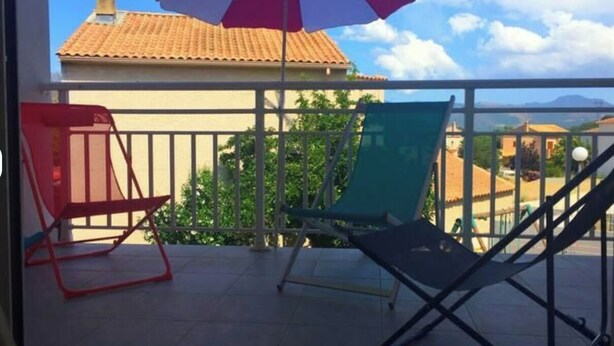 A balcony with two chairs, a red and white umbrella, and a view of buildings and trees. - Rental apartment T2, 53m2 à Corte in quiet residence (Corte)