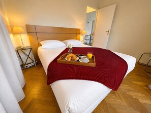 Quarto de hotel com cama, abajures, uma bandeja com croissants, café e suco, e um espelho na parede.