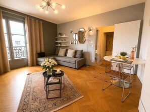 Ein Wohnzimmer mit einer Couch, einem Couchtisch mit Blumen, einem Essbereich mit Tisch und Stühlen und einem großen Fenster mit Vorhängen.