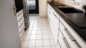 Una cocina moderna con armarios blancos, encimera negra y refrigerador de acero inoxidable.