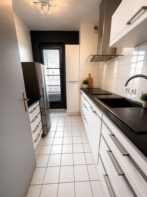 Eine moderne Küche mit weißen Schränken, einer schwarzen Arbeitsplatte und einem Edelstahl-Kühlschrank.