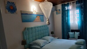Ein Schlafzimmer mit Bett, Nachttischen, einem Sessel, einer Lampe, einem Bild und einem Fenster mit Vorhängen.