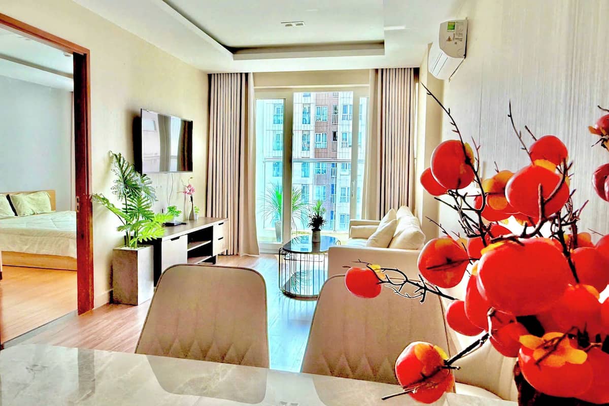 A modern hotel room with a bed, a desk, a dining area, and a large window with a city view.