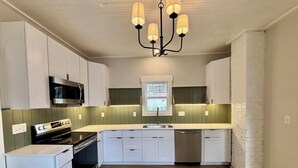 A kitchen with white cabinets, a built-in microwave, a stove, a dishwasher, and a chandelier. - Brooklyn Arts District Historic Home 1BR, 1BA (Wilmington)