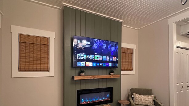 A living room with a flat-screen TV mounted on a wall, a fireplace below it, a green armchair, and a wicker basket on the floor. - Brooklyn Arts District Historic Home 1BR, 1BA (Wilmington)
