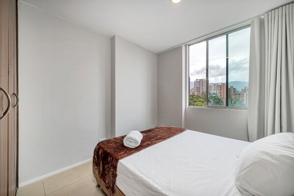 A hotel room with a bed, a window with curtains, and a view of buildings. - Poblado de Alejandr a - 1202 (Medellín)
