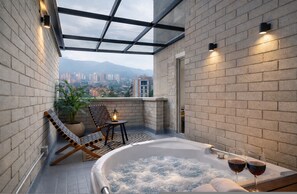 A modern balcony with a glass enclosure, a hot tub, lounge chairs, and a view of a cityscape. - Poblado de Alejandr a - 1202 (Medellín)