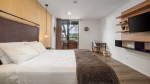 Une chambre moderne avec un grand lit, un bureau, une télévision et une vue sur l’extérieur grâce à une porte vitrée.