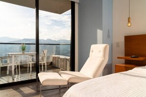 Un dormitorio moderno con una cama grande, un balcón con mesa y sillas, y vistas a las montañas.