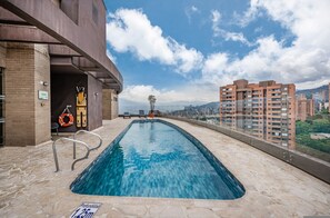 Una piscina en la azotea con vistas despejadas de la ciudad, un flotador salvavidas y un cartel que indica la profundidad de la piscina.