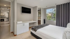 A modern hotel room with a bed, a flat-screen TV, a desk, and a view of the outdoors. - Cyan 703 - 2BR in Medell n (Medellín)