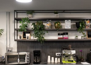 Eine Küche mit Kaffeemaschine, Toaster und Regalen mit Kaffeeverpackungen und Pflanzen.