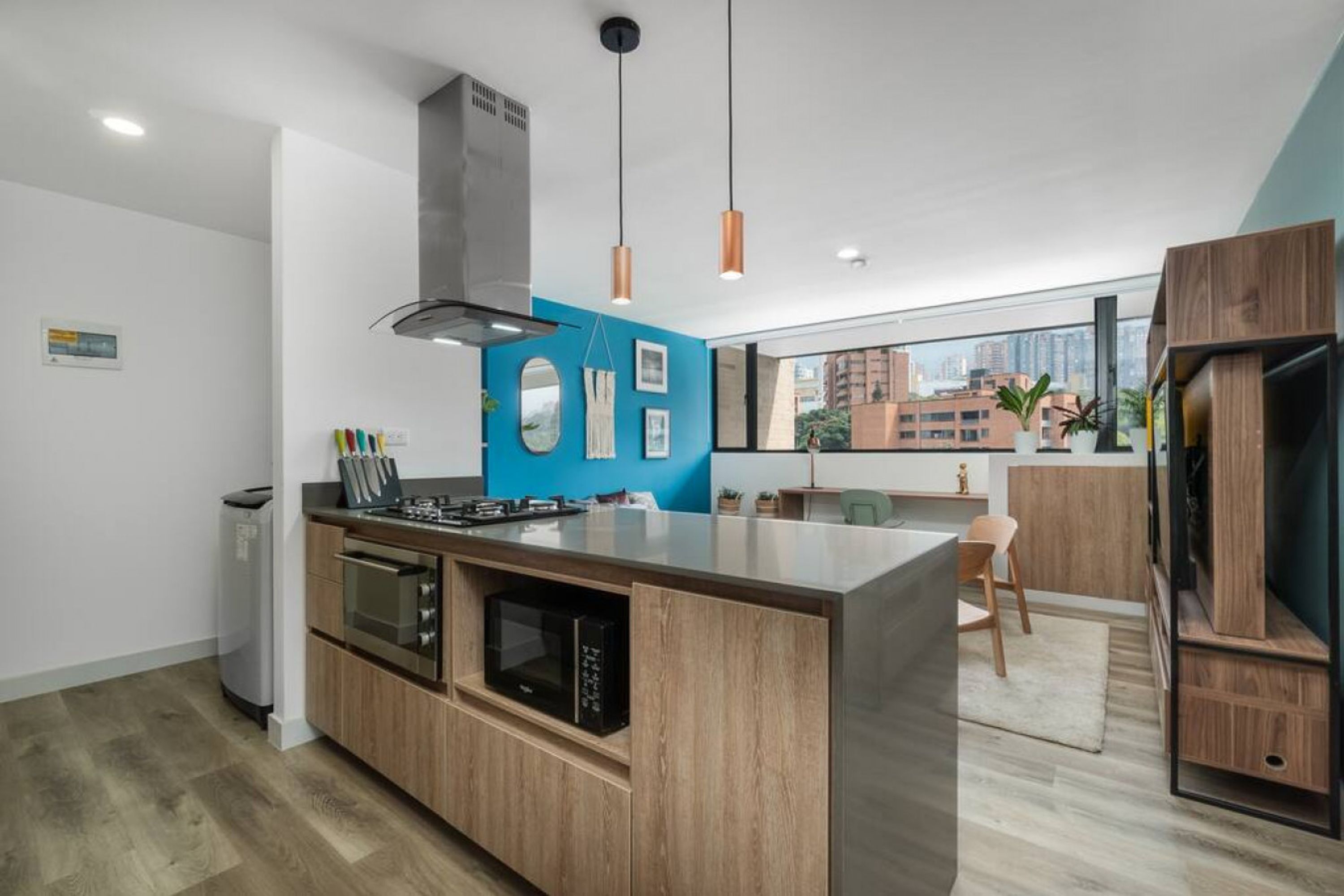 A modern kitchen with a central island, built-in oven, microwave, and a view of the city through large windows.