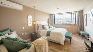 Une chambre moderne avec un grand lit, un canapé, un banc et une vue sur le paysage urbain, visible à travers de grandes fenêtres.