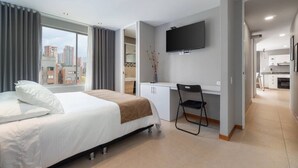 A hotel room with a bed, desk, chair, TV, and a view of the city. - Cyan 1001 - 2BR in Medell n (Medellín)