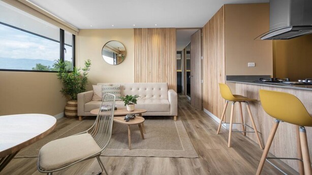 Ein modernes Wohnzimmer mit einer Couch, einem Couchtisch und Sesseln, einer Küchenzeile mit Herd und einem großen Fenster mit Blick.
