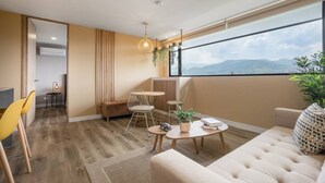 Ein modernes Wohnzimmer mit einer Couch, einem Couchtisch und einem Essbereich mit Stühlen. Ein großes Fenster bietet Blick auf die Berge.