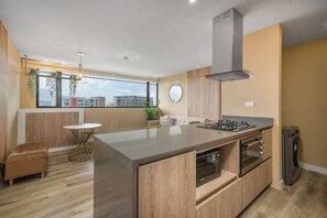 Eine moderne Küche mit einer zentralen Kochinsel, einem eingebauten Ofen und einem großen Fenster mit Blick auf die Stadt.