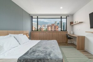 Una habitación de hotel moderna con una cama grande, un escritorio y vistas de la ciudad a través de amplios ventanales.