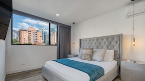 Ein modernes Schlafzimmer mit einem großen Bett, Blick auf Gebäude, einem grauen Kopfteil und einem Nachttisch.