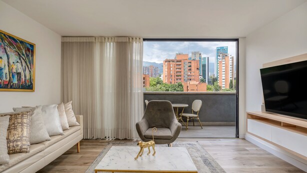Ein modernes Wohnzimmer mit Sofa, Couchtisch, Fernseher, Balkon mit Stadtblick und einem Bild an der Wand.