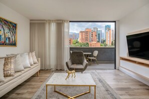 Een moderne woonkamer met een bank, een salontafel, een televisie, een balkon met uitzicht op de stad en een schilderij aan de muur.