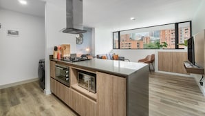 A modern kitchen with a central island, built-in oven, and a large window offering a city view. - Go Living Suites - 603 (Medellín)