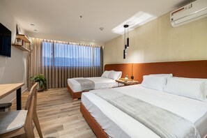 A hotel room with two beds, a desk, a chair, a potted plant, and a large window with curtains. - Go Living Suites - 1103 (Medellín)