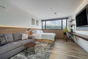 A modern bedroom with a large window, a bed, a desk, and a sofa. - Go Living Suites - 1015 (Medellín)