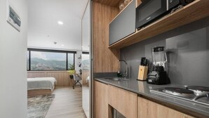 A modern kitchen with a view, wooden cabinets, a black microwave, a coffee maker, and a blender. - Go Living Suites - 1015 (Medellín)