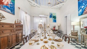 A dining room with a long table set for a meal, wooden cabinets, and artwork on the walls. - Amazing Colonial Mansion-8br-private Pool-old City (Cartagena)