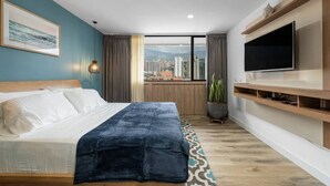 A bedroom with a bed, a TV, a plant, and a view of the city. - Go Living Suites - 1406 (Medellín)