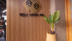 A reception area with a wooden panel wall, a logo, and the text 'HOLY HANDS SPA'. - Go Living Suites - 1407 (Medellín)