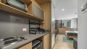A compact kitchenette with a stove, sink, and dish rack, a small refrigerator, and a window overlooking a cityscape. - Go Living Suites - 1407 (Medellín)