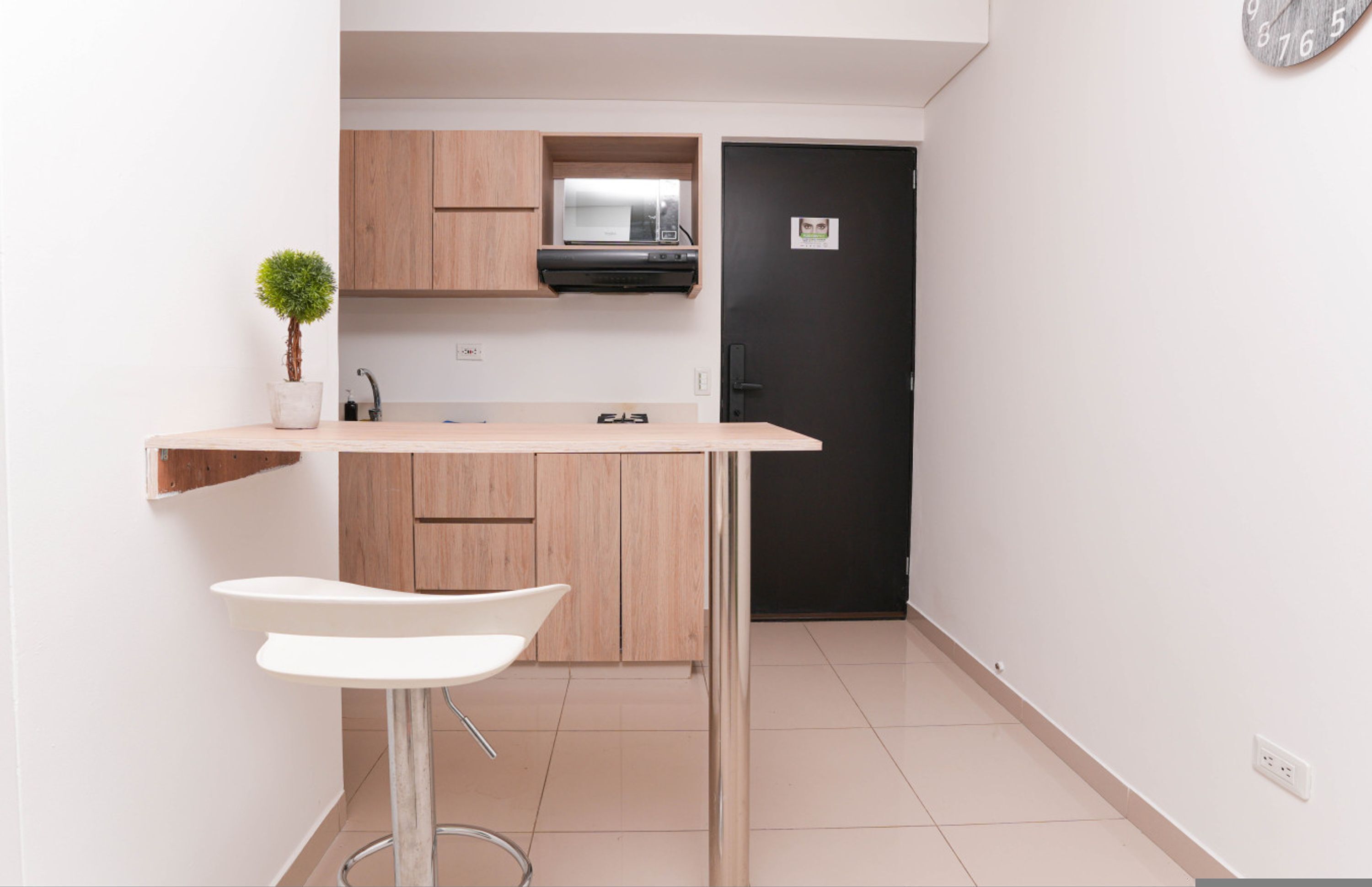 Cozinha compacta com armários de madeira, micro-ondas e porta preta.