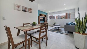 Un comedor con una mesa y sillas, un sofá, un televisor y una ventana con vistas a edificios.