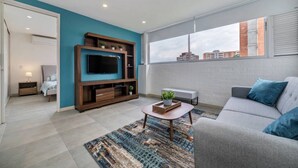 Una sala de estar moderna con un televisor de pantalla plana, un sofá, una mesa de centro y un amplio ventanal con vistas a la ciudad.