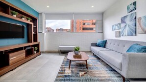 Una sala de estar moderna con un televisor de pantalla plana, un sofá gris, una mesa de centro y un ventanal con vistas a edificios.
