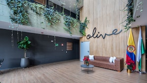 A lobby with a wooden wall, a sofa, a coffee table, potted plants, and flags. - Olive Country Living - 311 (Envigado)