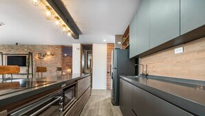 A modern kitchen with a brick accent wall, wooden cabinets, and a stainless steel refrigerator. - Olive Country Living - 311 (Envigado)