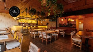 Ein Restaurantinnenraum mit Holztischen und -stühlen, einer Bar und hängenden Pflanzen.